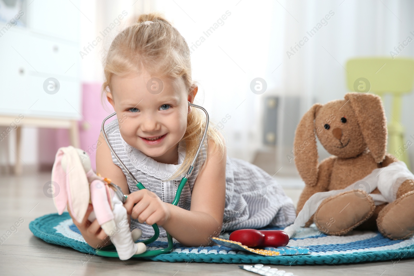 Photo of Cute child imagining herself as doctor while playing with stethoscope and toy bunny at home