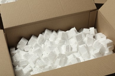 Photo of Open cardboard box with pieces of polystyrene foam, closeup. Packaging goods