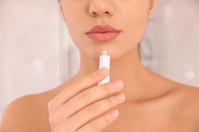 Photo of Woman with herpes applying cream on lips against blurred background, closeup