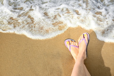 Photo of Closeup of woman with flip flops on sand near sea, space for text. Beach accessories