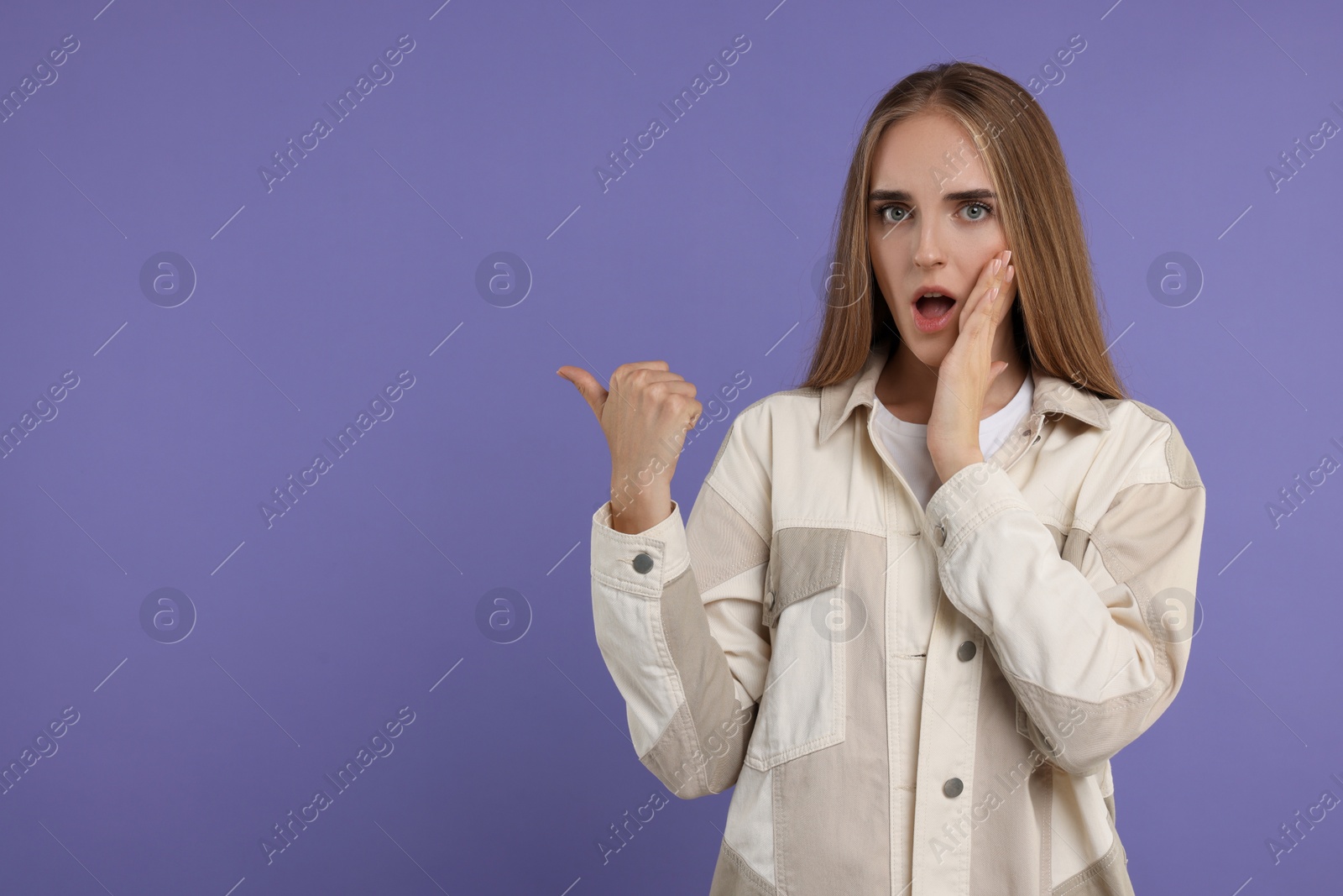 Photo of Special promotion. Emotional woman pointing at something on violet background, space for text