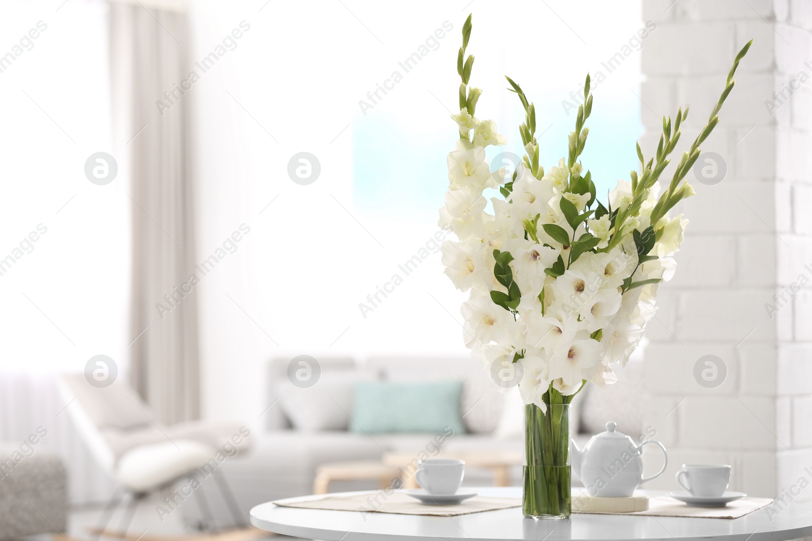 Photo of Vase with beautiful white gladiolus flowers on wooden table in living room. Space for text