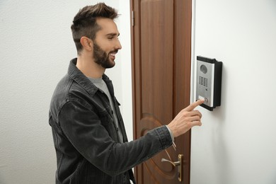 Photo of Happy man ringing intercom with camera in entryway