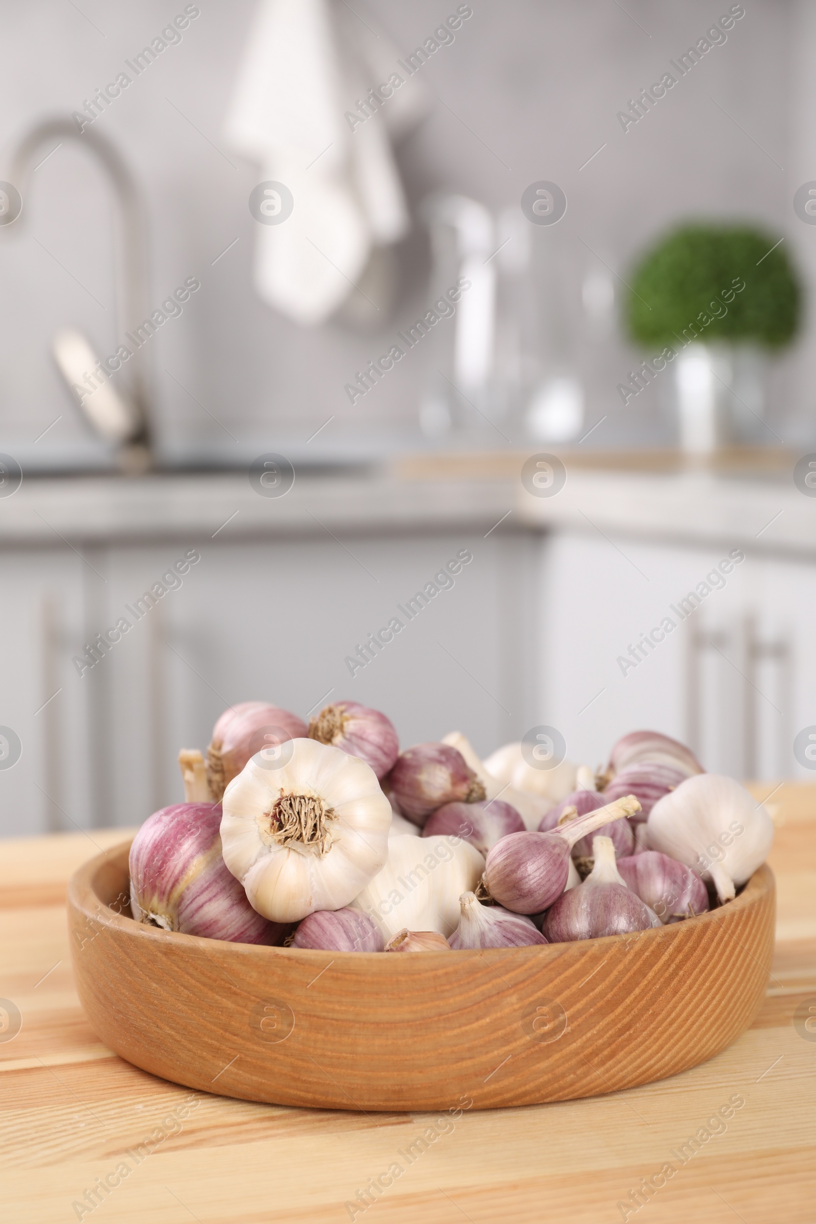 Photo of Bowl of fresh raw garlic on wooden table in kitchen, space for text