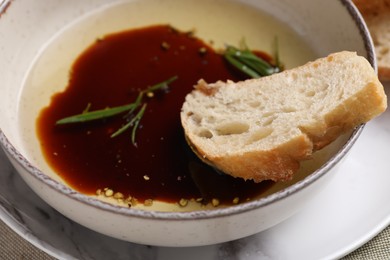 Photo of Balsamic vinegar with oil, rosemary and bread slice in bowl, closeup