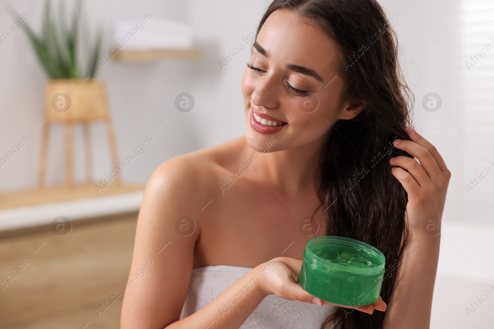 Photo of Happy young woman applying aloe hair mask indoors