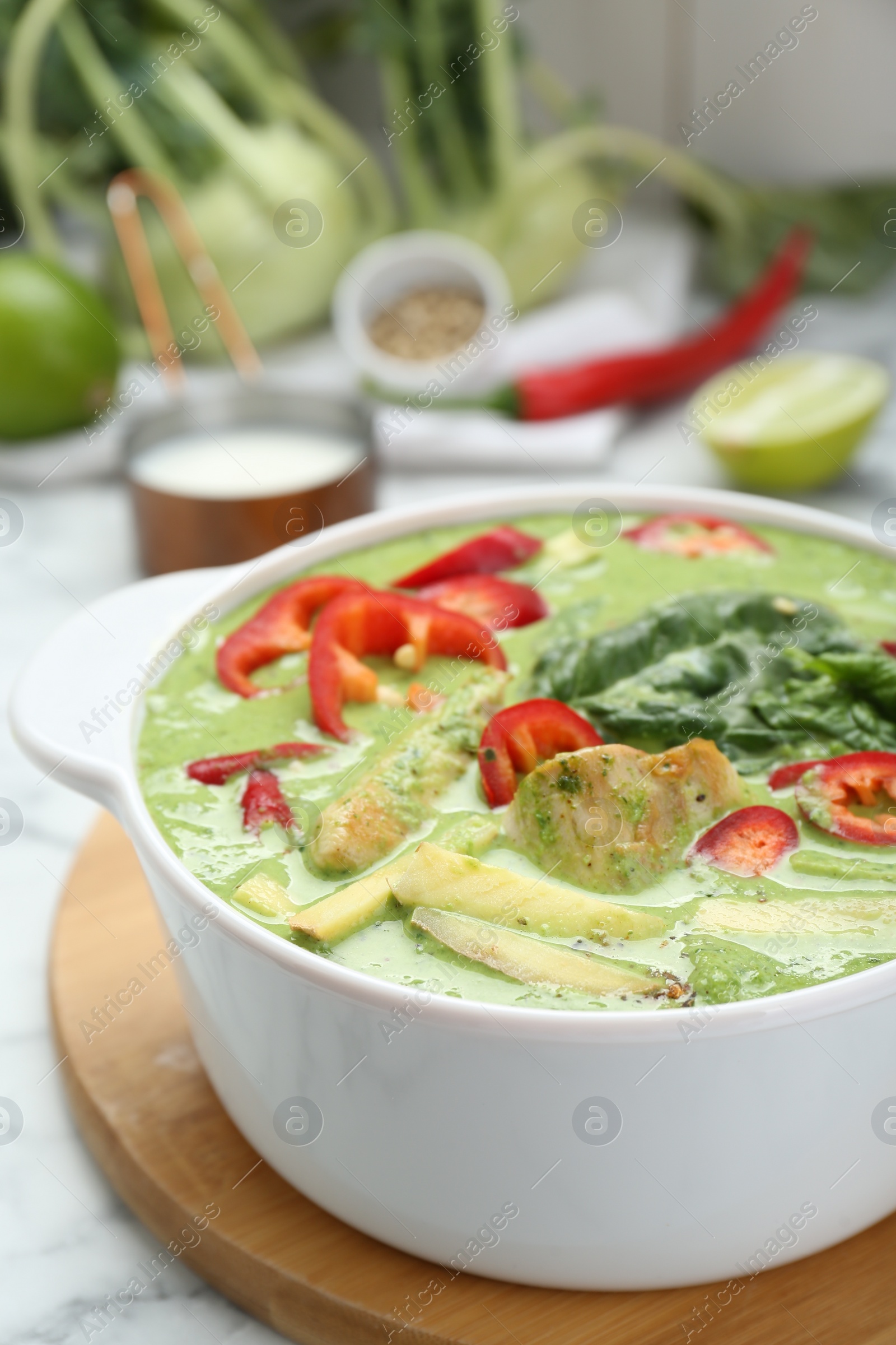 Photo of Saucepan with delicious green curry chicken soup on white marble table, closeup