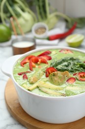 Saucepan with delicious green curry chicken soup on white marble table, closeup