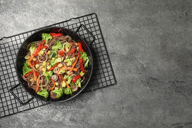 Photo of Stir fried noodles with mushrooms and vegetables in wok on grey table, top view. Space for text