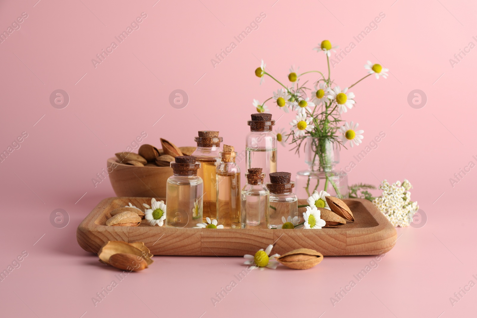 Photo of Aromatherapy. Different essential oils, flowers and almonds on pink background