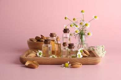 Aromatherapy. Different essential oils, flowers and almonds on pink background