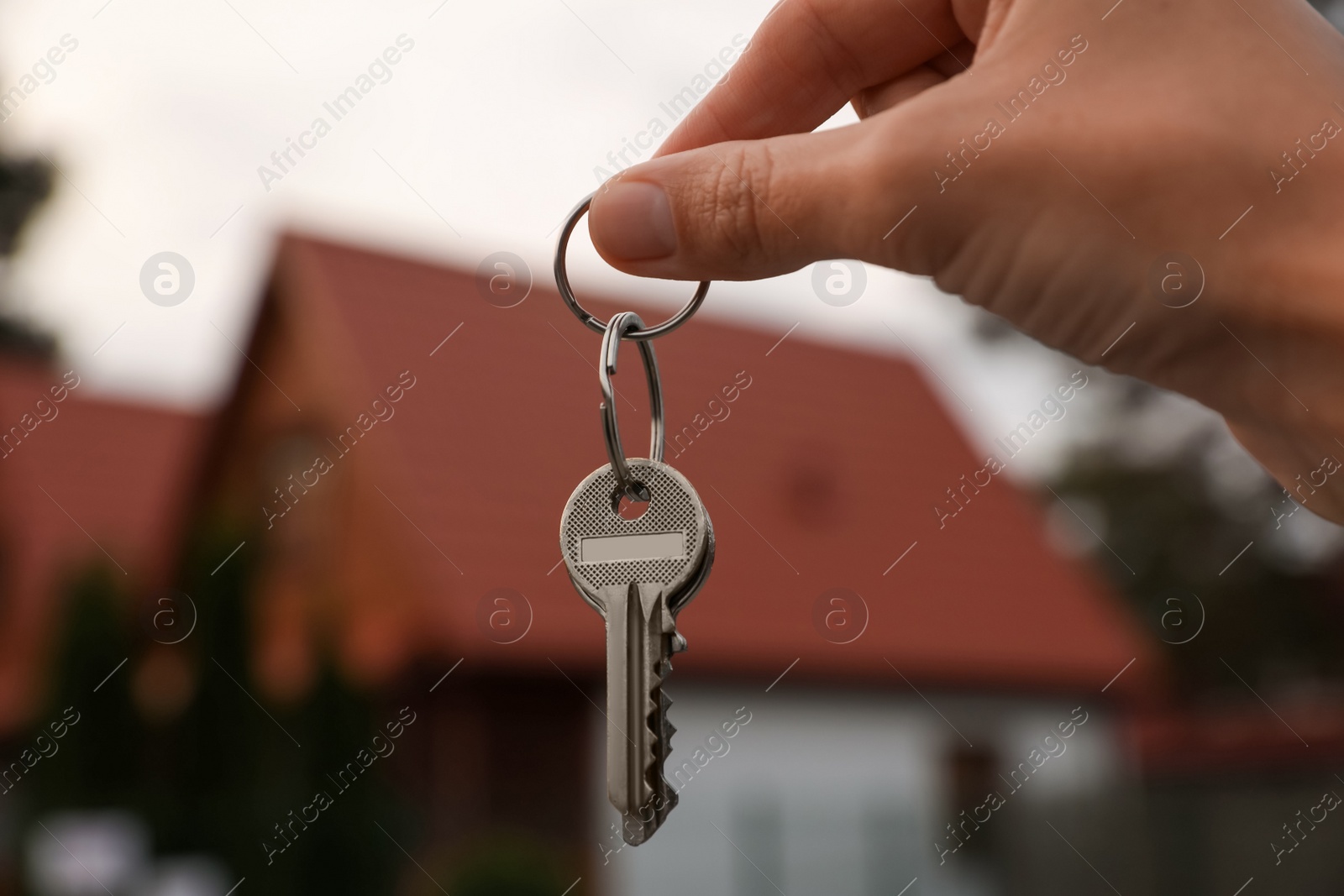 Photo of Real estate agent holding keys to new house outdoors, closeup