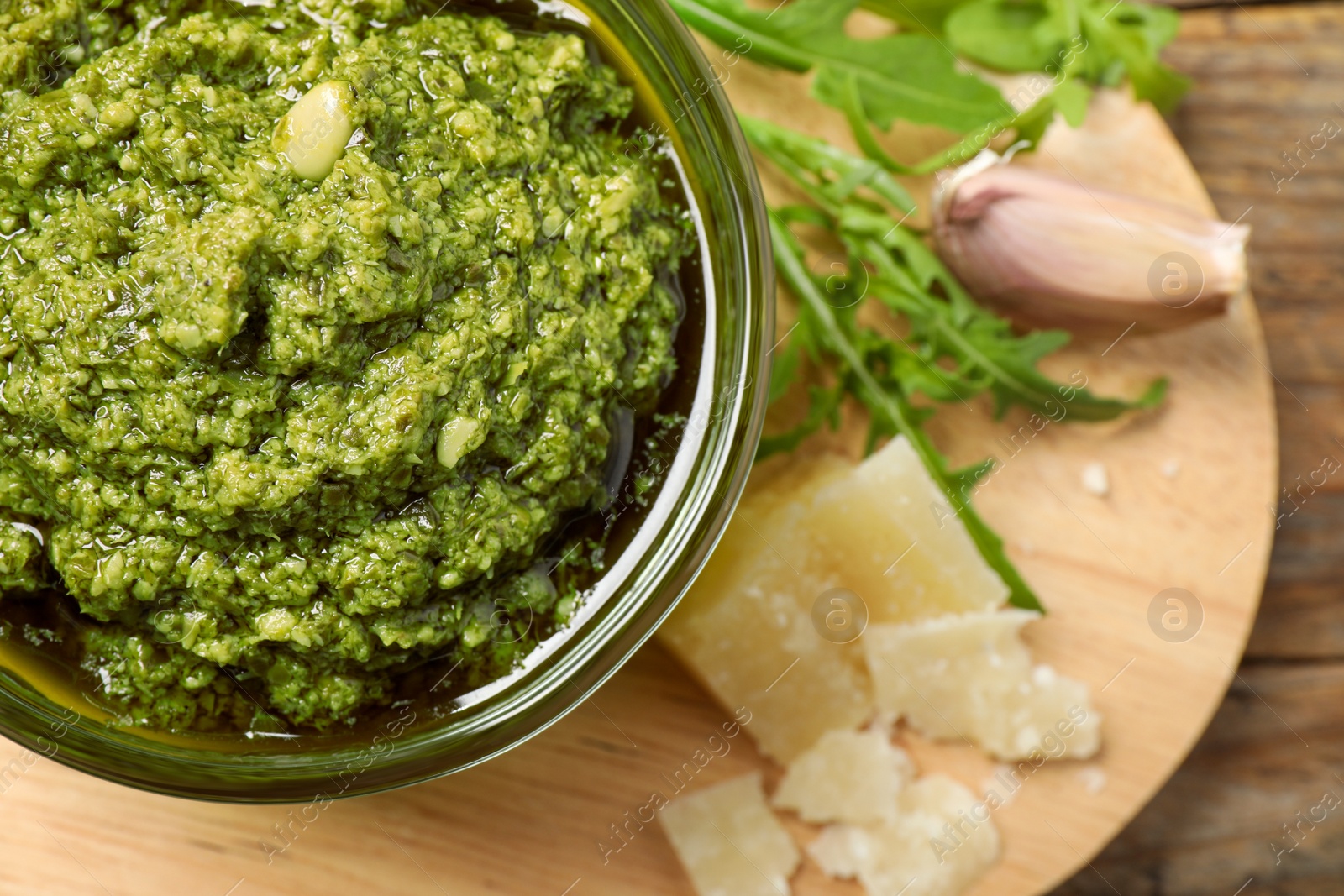 Photo of Bowl of tasty arugula pesto and ingredients on wooden board, flat lay