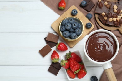 Photo of Fondue pot with chocolate and different berries on white wooden table, flat lay. Space for text