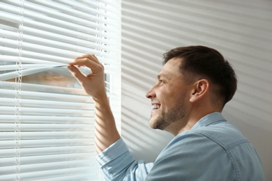 Photo of Handsome man opening window blinds at home