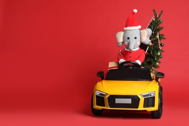 Child's electric car with toys, gift boxes and Christmas tree on red background, space for text