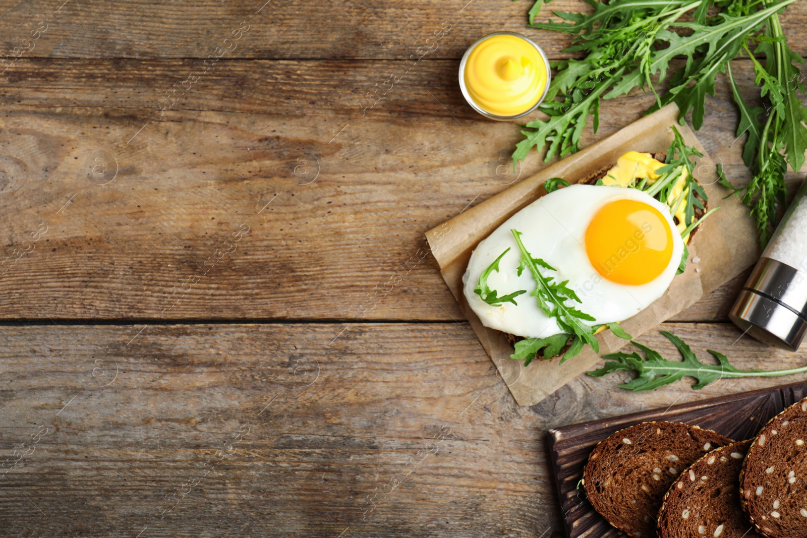 Photo of Delicious sandwich with arugula and egg on wooden table, flat lay. Space for text
