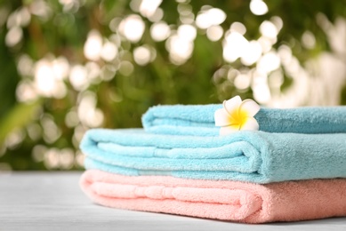 Photo of Pile of fresh towels and flower on table against blurred background, space for text