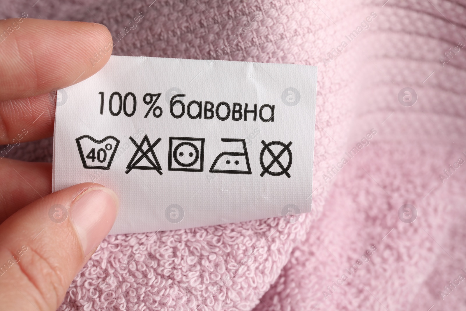 Photo of Woman holding clothing label on pink fluffy towel, closeup