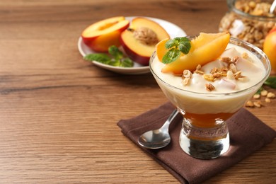Photo of Tasty peach yogurt with granola, mint and pieces of fruit in dessert bowl on wooden table, space for text