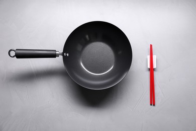 Empty iron wok and chopsticks on grey table, flat lay