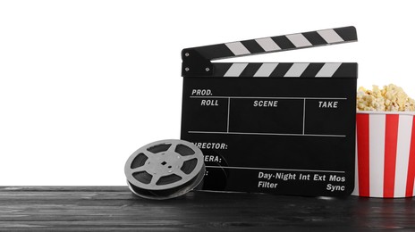 Photo of Movie clapper, bucket of tasty popcorn and film reel on wooden table against white background, space for text