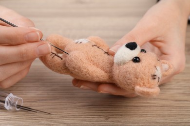 Photo of Woman felting cute toy bear from wool at wooden table, closeup