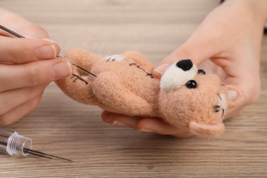 Woman felting cute toy bear from wool at wooden table, closeup