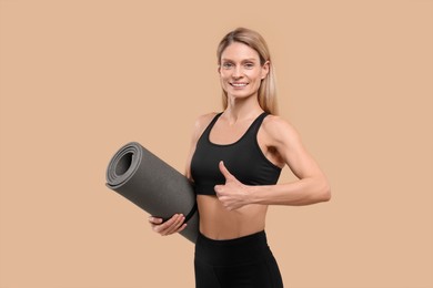 Photo of Athletic woman with fitness mat showing thumbs up on beige background