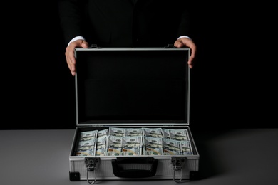 Photo of Businessman with suitcase full of money on dark background