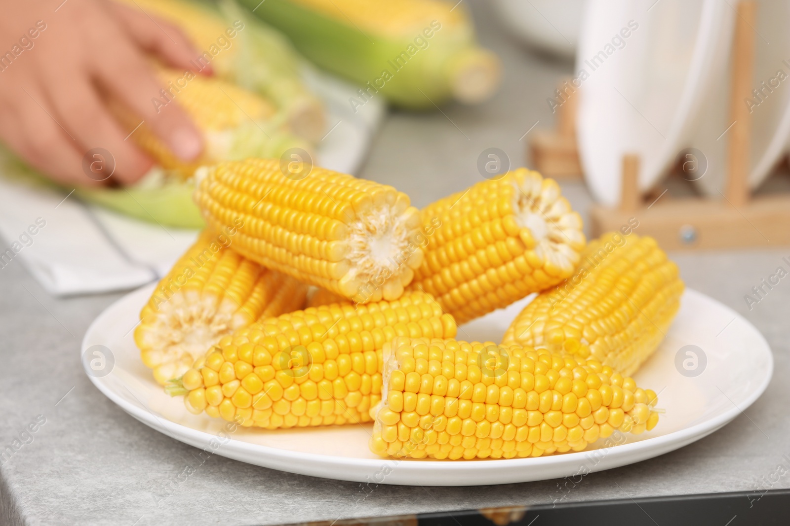 Photo of Plate with ripe corn cobs and blurred woman on background