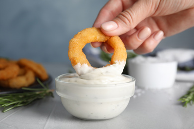 Woman dipping crunchy fried onion ring in sauce, closeup