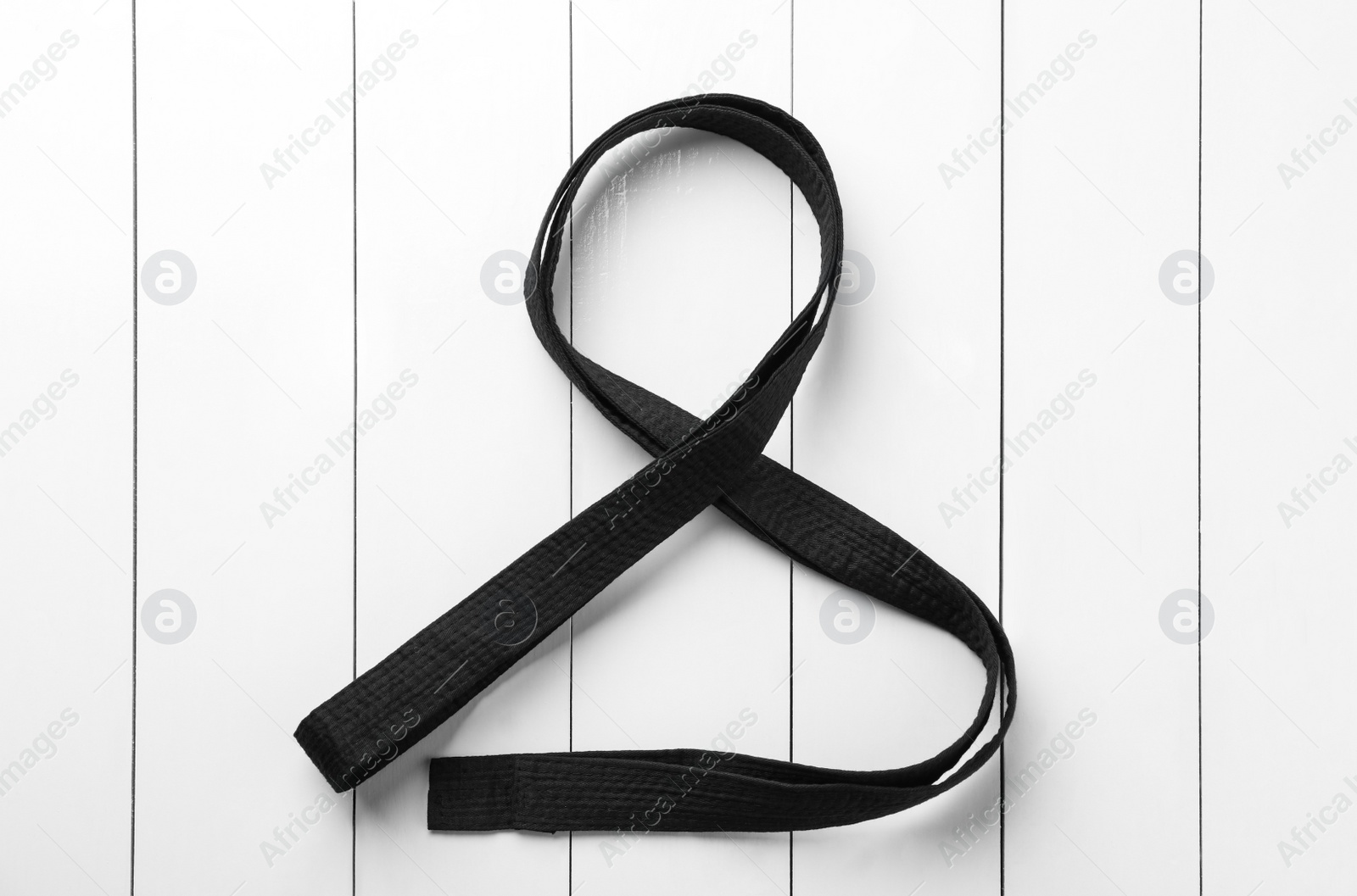 Photo of Black belt on white wooden background, top view. Oriental martial arts