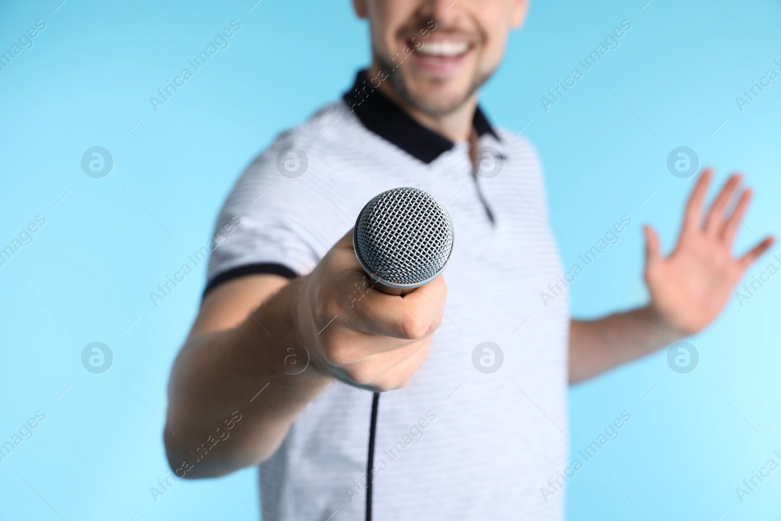 Photo of Handsome man in casual clothes holding microphone on color background, closeup