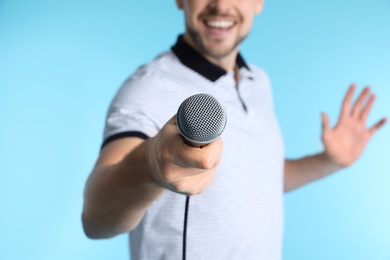 Handsome man in casual clothes holding microphone on color background, closeup