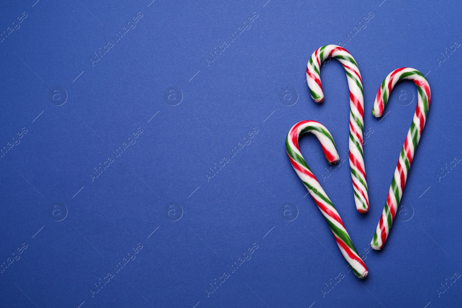 Photo of Many sweet Christmas candy canes on blue background, flat lay. Space for text