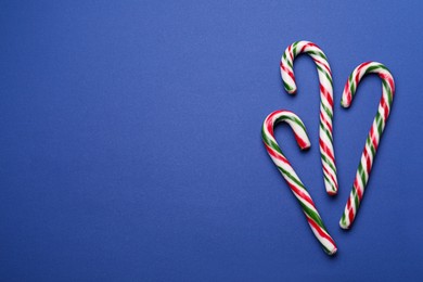 Photo of Many sweet Christmas candy canes on blue background, flat lay. Space for text