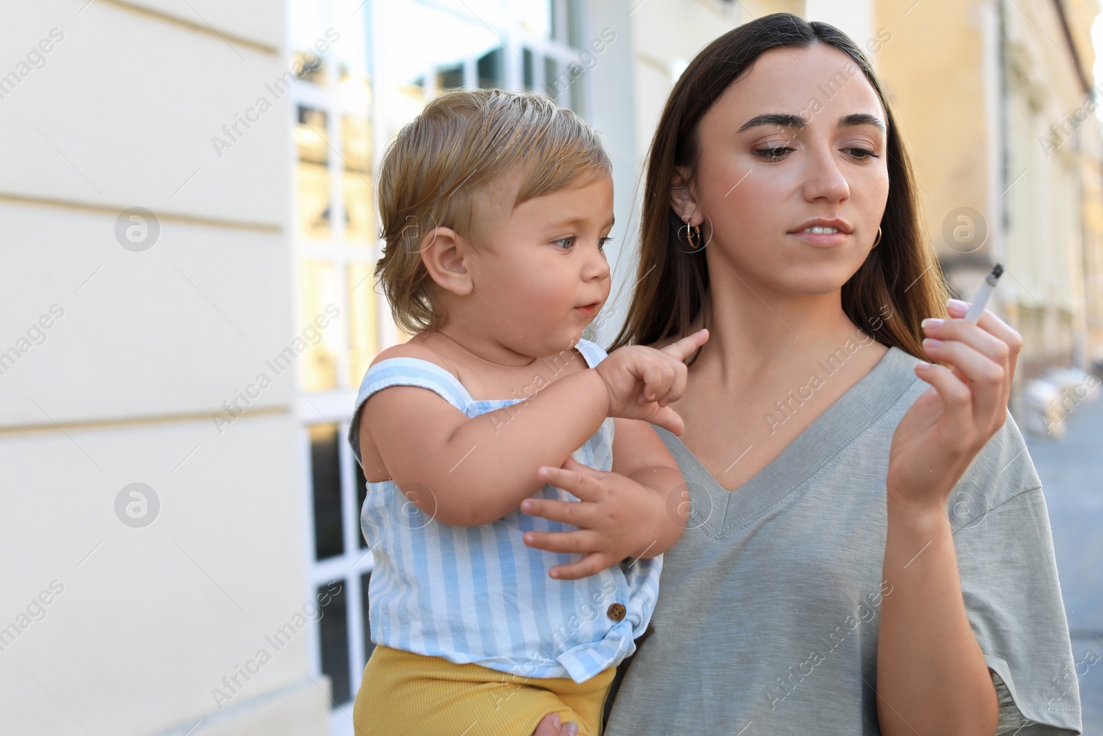 Photo of Mother with cigarette and child outdoors. Don't smoke near kids