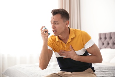 Photo of Young man with asthma inhaler on bed in light room