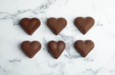 Photo of Tasty heart shaped chocolate candies on white marble table, flat lay. Happy Valentine's day