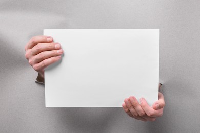 Photo of Man holding sheet of paper through holes in white paper, closeup. Mockup for design