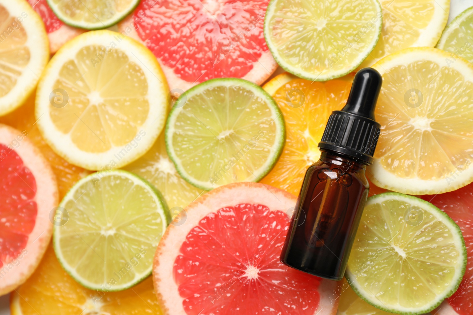 Photo of Bottle of essential oil on pile of citrus slices, flat lay. Space for text