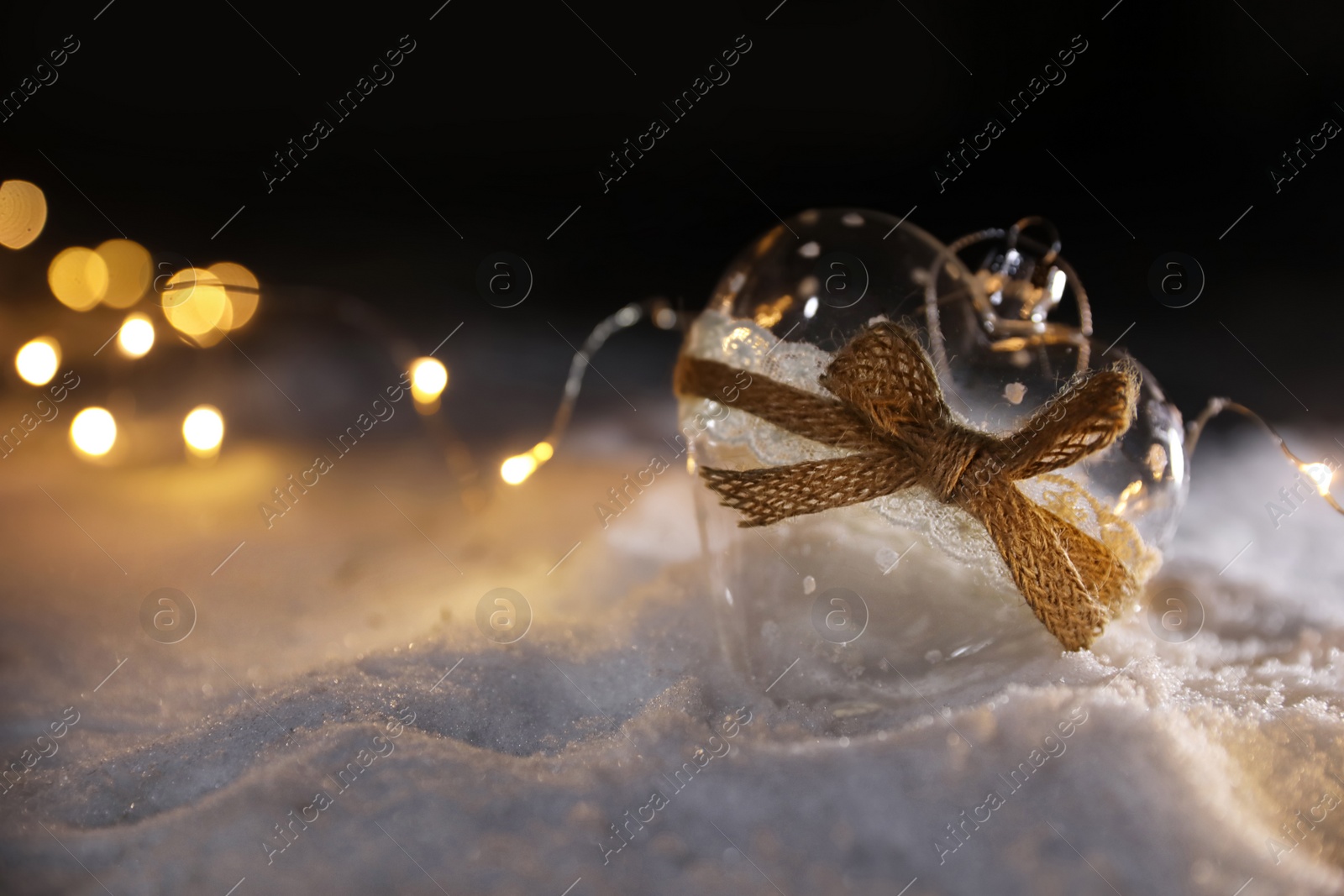 Photo of Glass heart and fairy lights on white snow outdoors. Space for text