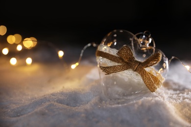 Photo of Glass heart and fairy lights on white snow outdoors. Space for text