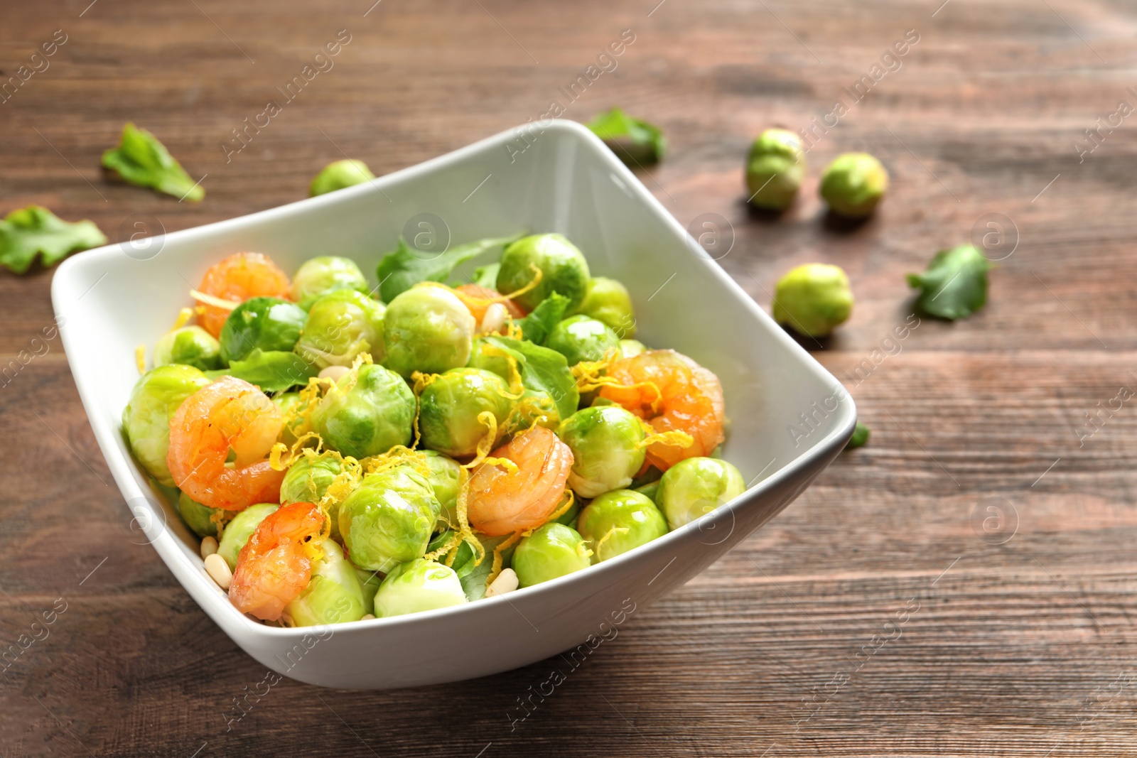 Photo of Bowl of delicious salad with Brussels sprouts and shrimps on wooden table