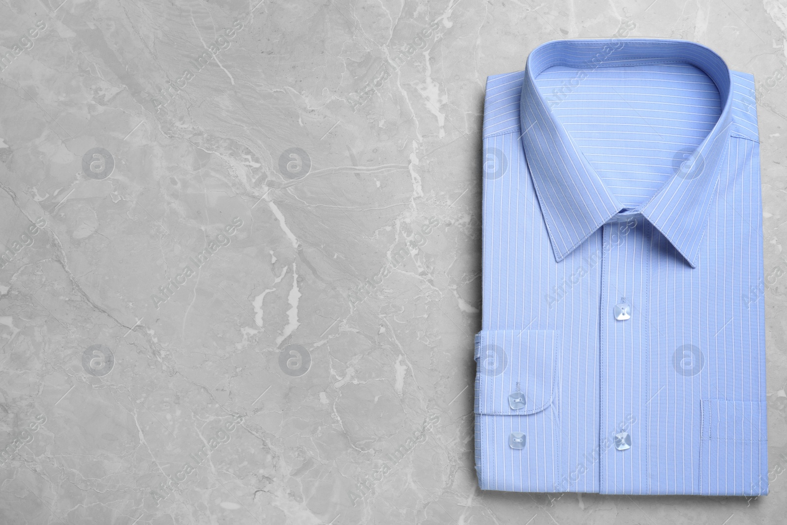 Photo of Stylish light blue shirt on grey marble table, top view with space for text. Dry-cleaning service