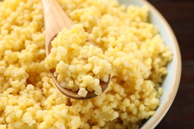 Photo of Tasty millet porridge and spoon in bowl on table, closeup