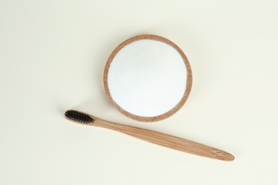 Bamboo toothbrush and bowl with baking soda on beige background, flat lay