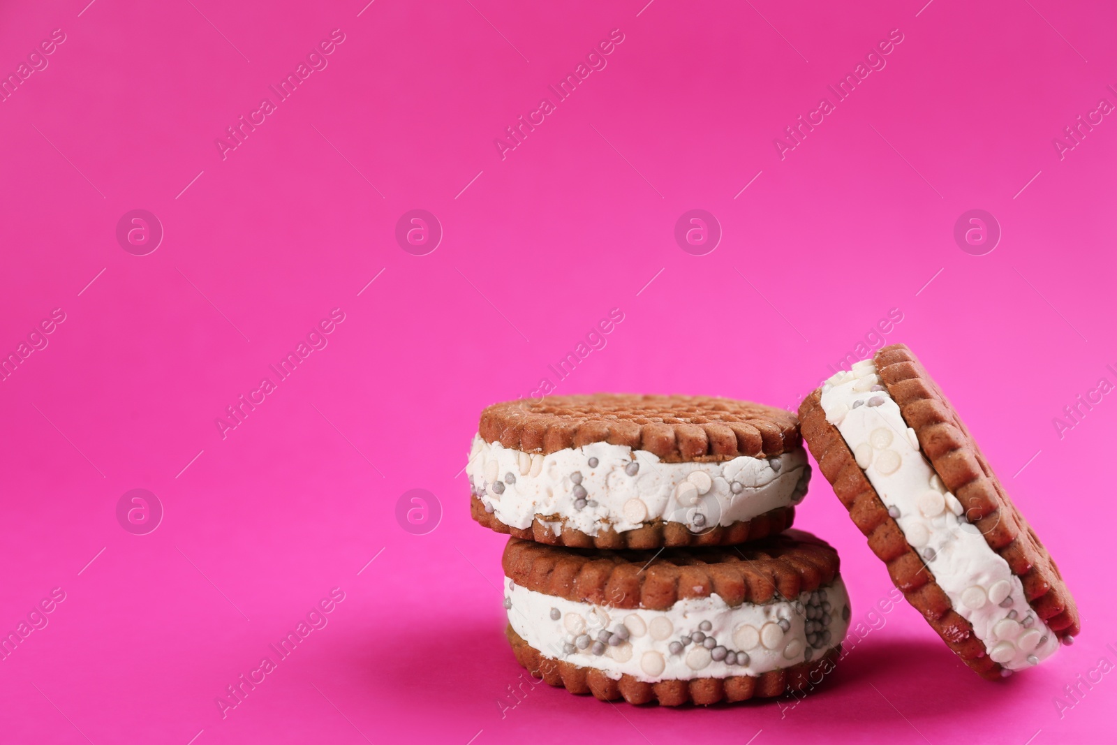 Photo of Sweet delicious ice cream cookie sandwiches on pink background. Space for text