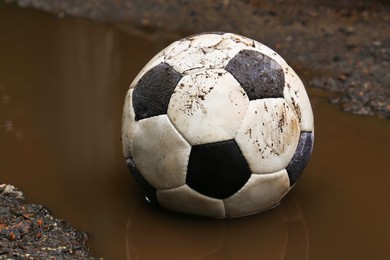 Photo of Dirty soccer ball in muddy puddle, closeup